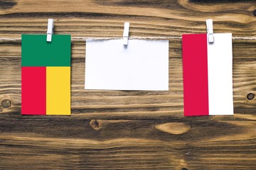 Hanging flags of Benin and Poland attached to rope with clothes pins with copy space on white note paper on wooden background.Diplomatic relations between countries.