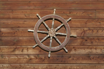 Old ship steering wheel hangs on the wooden wall