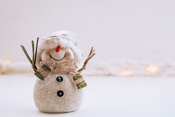 Single white cheerful snowman smiling and standing on a background with snow and lights