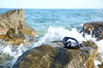 Fototapeta na wymiar black wet diving mask is on the stone in the ocean on the background of splashes of water