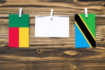 Hanging flags of Benin and Tanzania attached to rope with clothes pins with copy space on white note paper on wooden background.Diplomatic relations between countries.