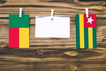 Hanging flags of Benin and Togo attached to rope with clothes pins with copy space on white note paper on wooden background.Diplomatic relations between countries.