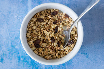 Breakfast granola cereal bowl with fruit and spoon on minimal blue food background