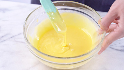 Mixing egg yolk into cake batter with green rubber spatula mixer tool stirring until smooth and blend well in a glass bowl, close up, lifestyle