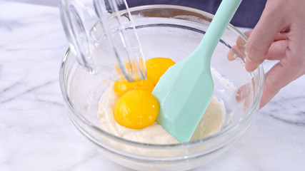 Mixing egg yolk into cake batter with green rubber spatula mixer tool stirring until smooth and blend well in a glass bowl, close up, lifestyle