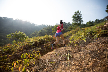 Woman trail runner running up on mountain slope in tropical forest