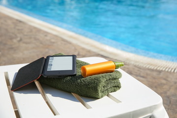 Conceptual photo of towel, sunblock and e-book against the background of the pool.