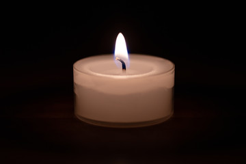 Fototapeta na wymiar Closeup of a candle on a wooden table with dark background - center