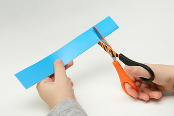 child's hands scissor a strip of blue paper on white background. child scissors color paper.