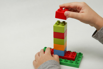 hands of the child lay a pyramid of colorful cubes on white background. child plays construction set