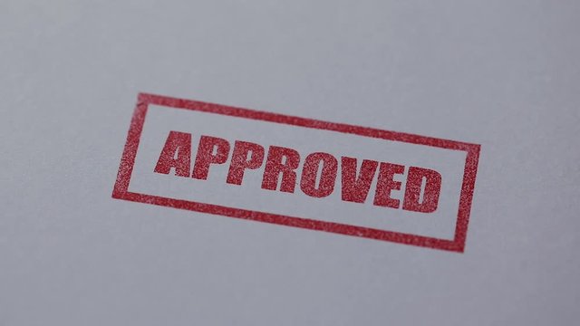 hand put a red approved stamp on white paper