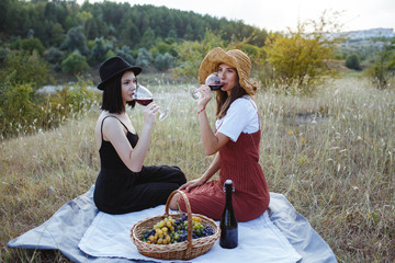Two brunette girls serve wine on a field at sunset.