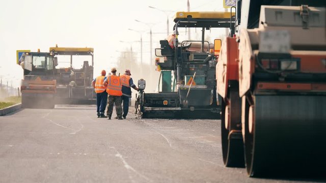 Workers and rolling machines lay asphaly on a road.