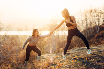 The girl helps her friend with jogging outdoors in the sun. Female Friendship and care.