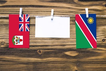 Hanging flags of Bermuda and Namibia attached to rope with clothes pins with copy space on white note paper on wooden background.Diplomatic relations between countries.