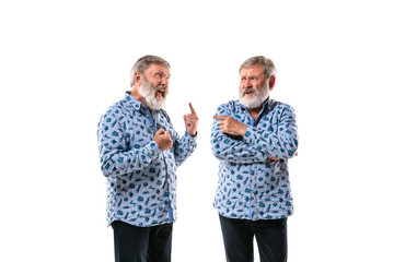 Senior man arguing with himself on white studio background. Concept of human emotions, expression, mental issues, internal conflict, split personality. Half-length portrait. Negative space. Pointing.