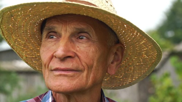 old man in straw hat with smile on face looks up in sky and around countryside garden slow motion close view