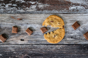 Freshly baked, home made chocolate chip cookie seen together with a chunk for cooking chocolate on a wooden, kitchen surface work to