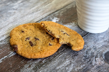 Freshly prepared chocolate chip cookies, partially eaten seen on a wooden kitchen surface together with a coffee mug.
