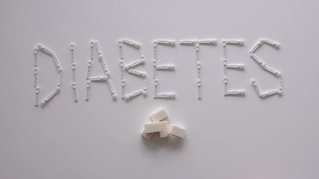 The word DIABETES with lancets for glucometer on the table on a white background. Lay next to the sugar cubes. A woman's hand takes a sugar cube. The concept of type 1 and type 2 diabetes.