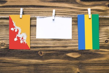 Hanging flags of Bhutan and Gabon attached to rope with clothes pins with copy space on white note...