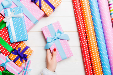Obraz premium Top view of a woman holding a gift box in her hands on festive wooden background. Rolled up wrapping paper and Christmas decorations. New year time concept