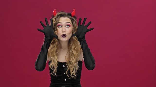 Beautiful and crazy devil woman in carnival costume flirting and having fun isolated over red wall background