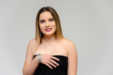 Fototapeta premium Studio portrait of a beautiful girl with long beautiful hair and excellent make-up on a gray background in different poses. She smiles.