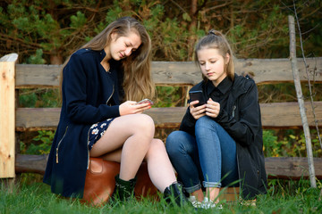 Two young girls are waiting, sitting on a suitcase and a stack of books on the nature.