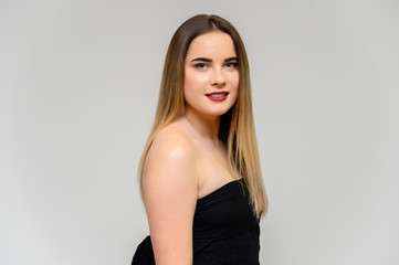 Fototapeta premium Studio portrait of a beautiful girl with long beautiful hair and excellent make-up on a gray background in different poses. She smiles.
