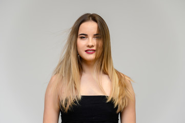 Fototapeta premium Studio large photo portrait of a beautiful girl with long beautiful flowing hair and excellent make-up on a gray background in different poses. She smiles.