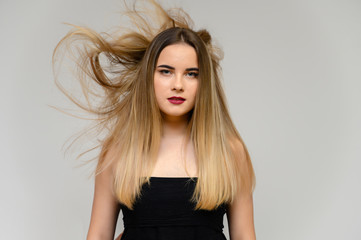 Studio large photo portrait of a beautiful girl with long beautiful flowing hair and excellent make-up on a gray background in different poses. She smiles.