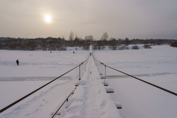 Cold snow white Russian winter. River Desna had been covered by ice and snow. Wooden suspension bridge. Fish men on the ice. The concepts of beauty of nature and ecological tourism.
