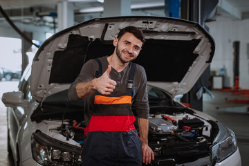 Obraz na płótnie Canvas In a modern auto service center closeup to the camera mechanic man charismatic showing big like and smile cute