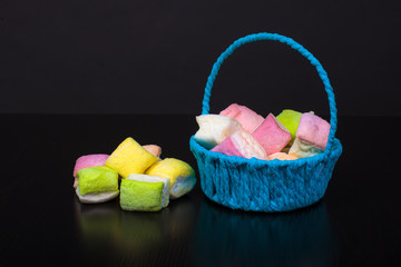 multicolored marshmallow in a blue basket on a black table