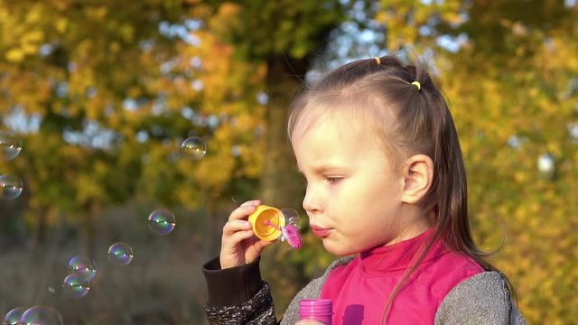 Beautiful little girl child blows soap bubbles. Plays in the autumn park. Slow motion.