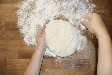 female hands knead the dough on a wooden table, sprinkled with flour, close-up, selective focus, home cooking concept, copy space