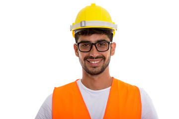 Studio shot of young happy Persian man construction worker smili