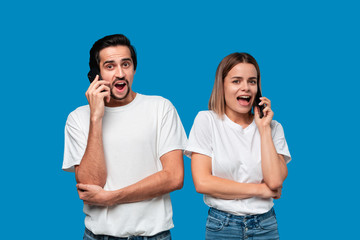 Blond woman and brunet man in white tees and blue jeans are surprised talking on the phone.