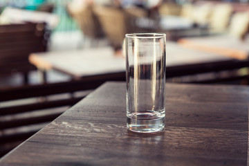 Empty transparent cylindrical glass over wooden table at restaurant, outdoor terrace, extreme...
