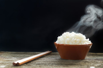 Jasmine rice in a bowl near by chopsticks. Selective focus steaming hot cooked rice in white bowl on black background.