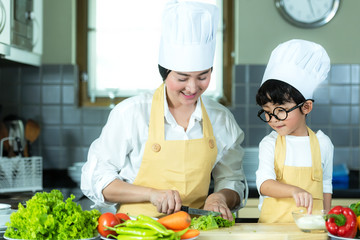 Healthy Family. Mother and kid boy cooking and cutting vegetables for diet on kitchen.  Smiling son...