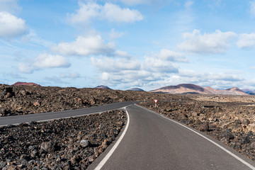 empty asphalt road road through arid volcanic landscape against blue sky
