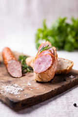 Sandwich with smoked pork sausage. Composition with fresh herbs and salt on a wood cutting board on a kitchen worktop.