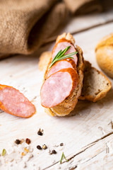 Sandwich with smoked pork sausage on a kitchen worktop. Composition with fresh rosemary, salt crystals and pepper.