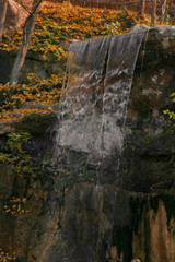 Fototapeta premium Waterfall from stones in the park. Against the background of autumn foliage and trees of orange and yellow.