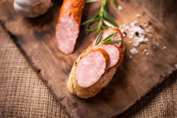Sandwich with smoked pork sausage. Rustic composition with fresh herbs, salt, aged wood cutting board and jute fabric.