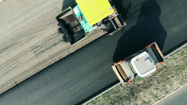 One roller rides on a road, laying asphalt.