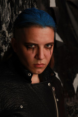 Teen alt boy with blue hair and shaved head dressed in black on dark background