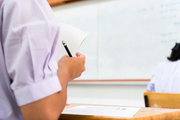 Education test exam in school concept : University student holding pencil notes paper on answer sheet at lecture whiteboard for taking exams in examination classroom. Assessment learning in class